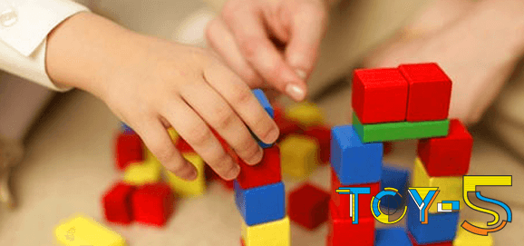 Детские руки собирают красочные кубики деревянного конструктора